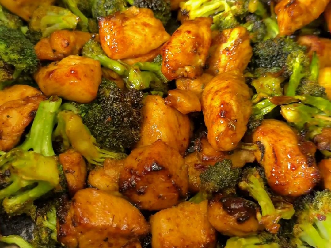Glazed honey sweet chili chicken pieces and charred broccoli florets in an air fryer basket